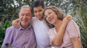 A smiling older white man and woman with a young brunette boy between them with his arms around their shoulders,